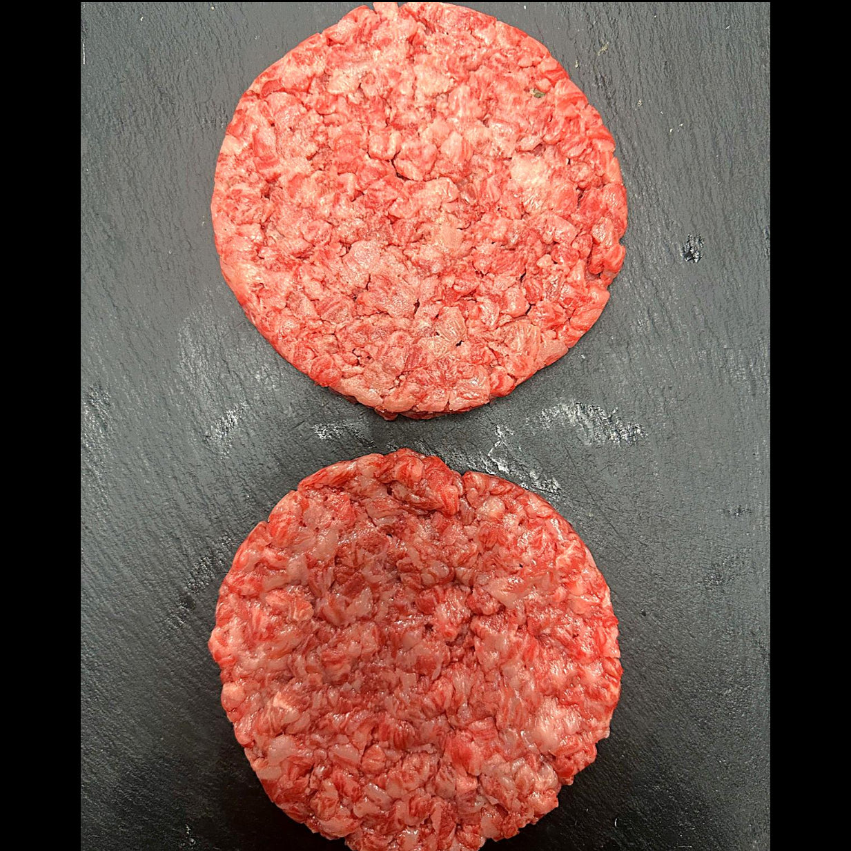 Two raw hamburger patties on a dark surface